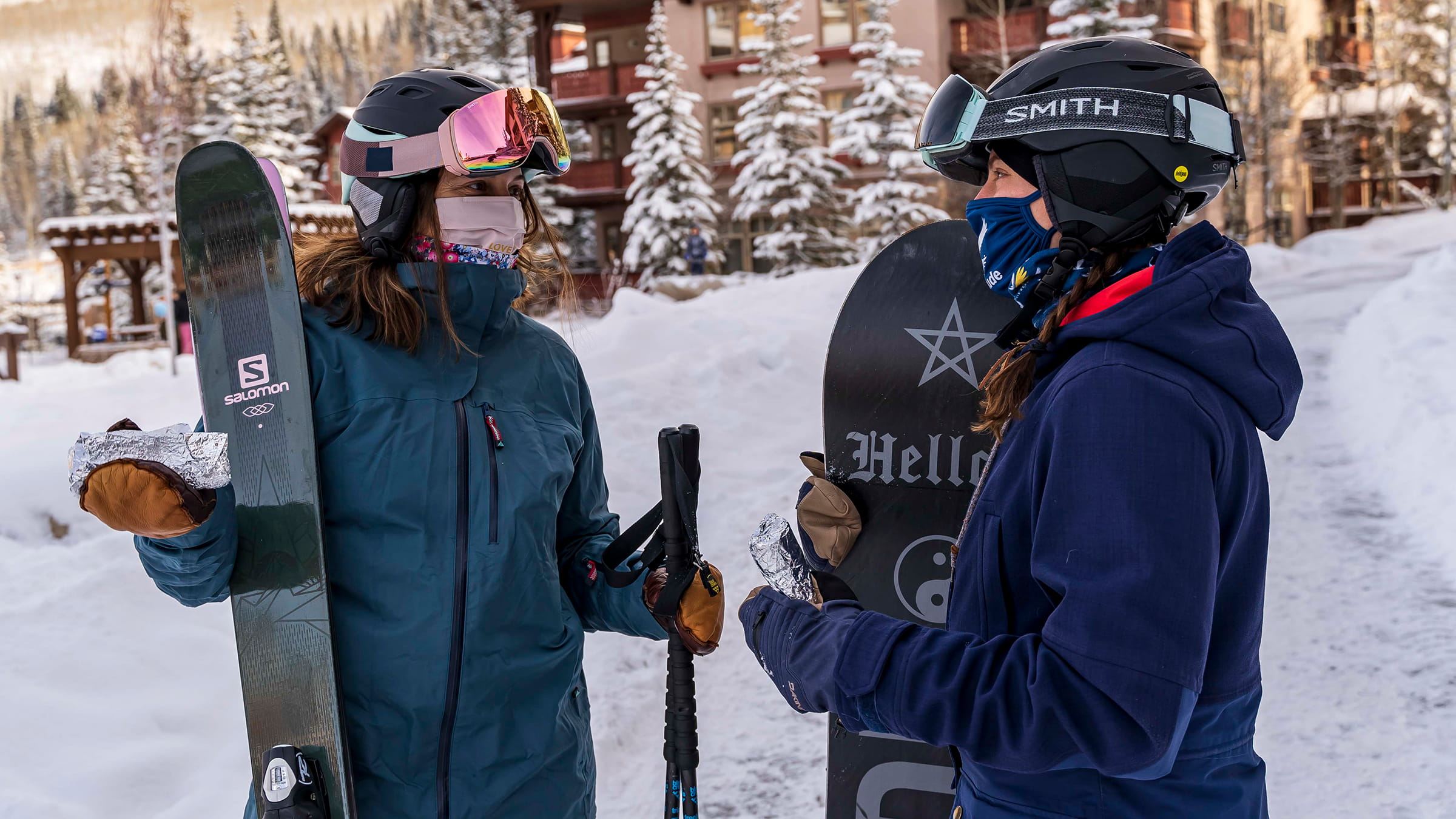 Snowboarder and skier chat outside at Solitude Village with masks on
