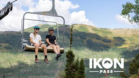 Two friends riding the chairlift at Solitude Mountain Resort with Ikon Pass logo