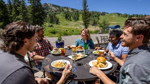 Friends dining outside at Honeycomb Grill with Apex Express in the background at Solitude Mountain Resort