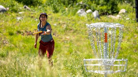 A female throwing a disc toward the basket at Solitude Mountain Resorts disc golf course. 