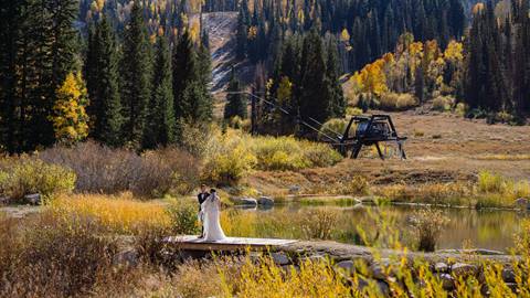 wide view of a couple standing on a dock surrounded by autumn trees and alpine scenery at a wedding venue at solitude mountain resort