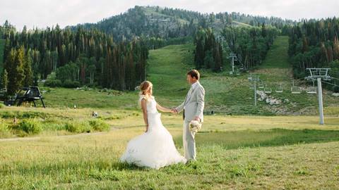 bride and groom holding hands in a mountain meadow with ski lifts at a wedding venue at solitude mountain resort