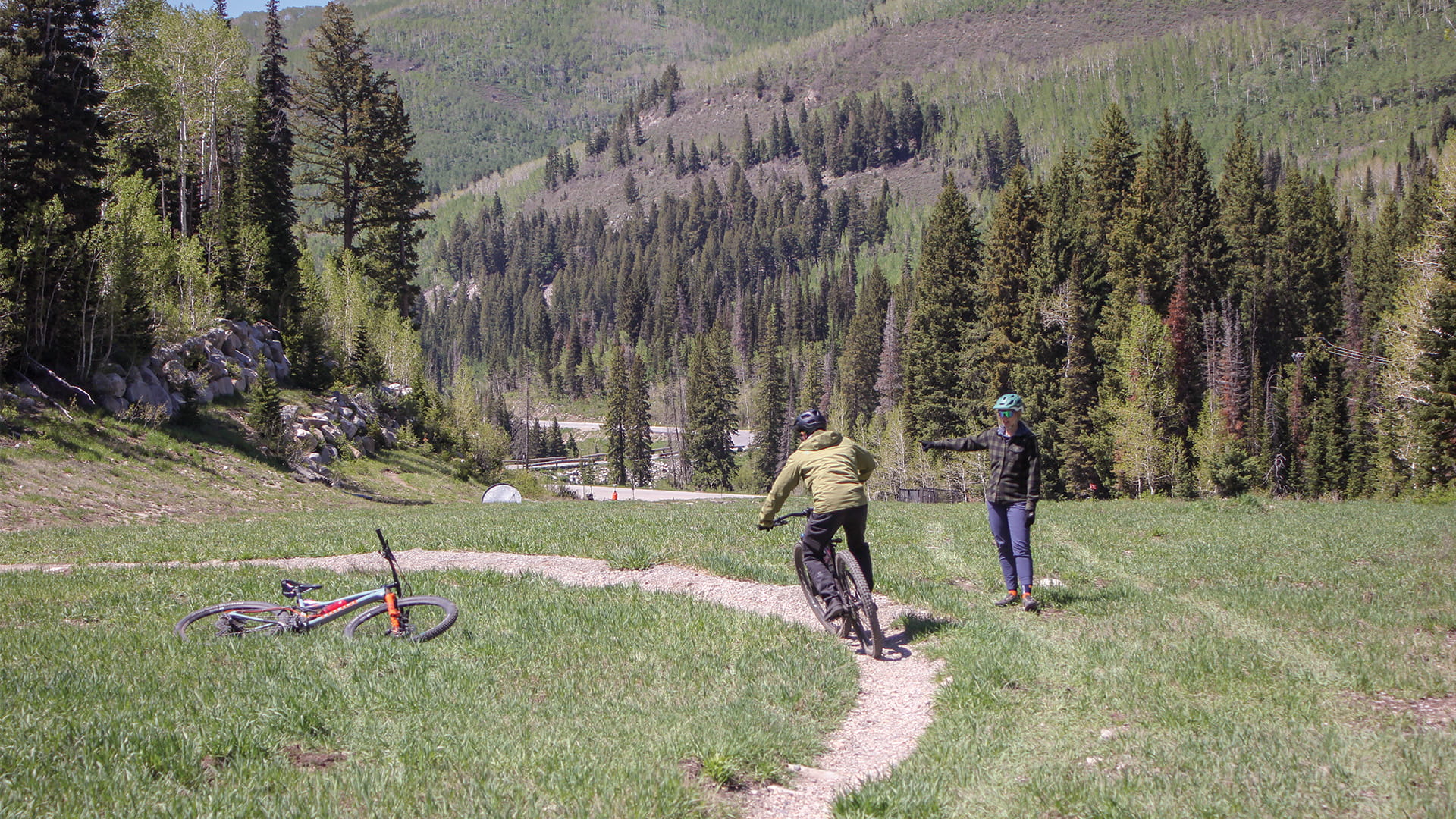 Mountain biker turning on a bike trail with instructor looking on