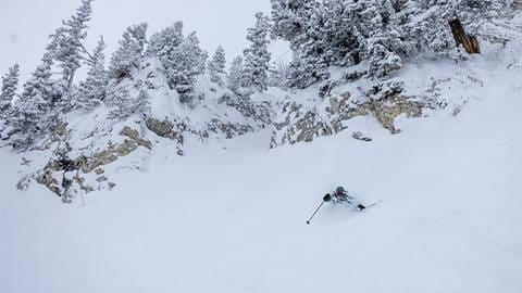 Skier in chest deep powder with a cliff and chairlift in the background