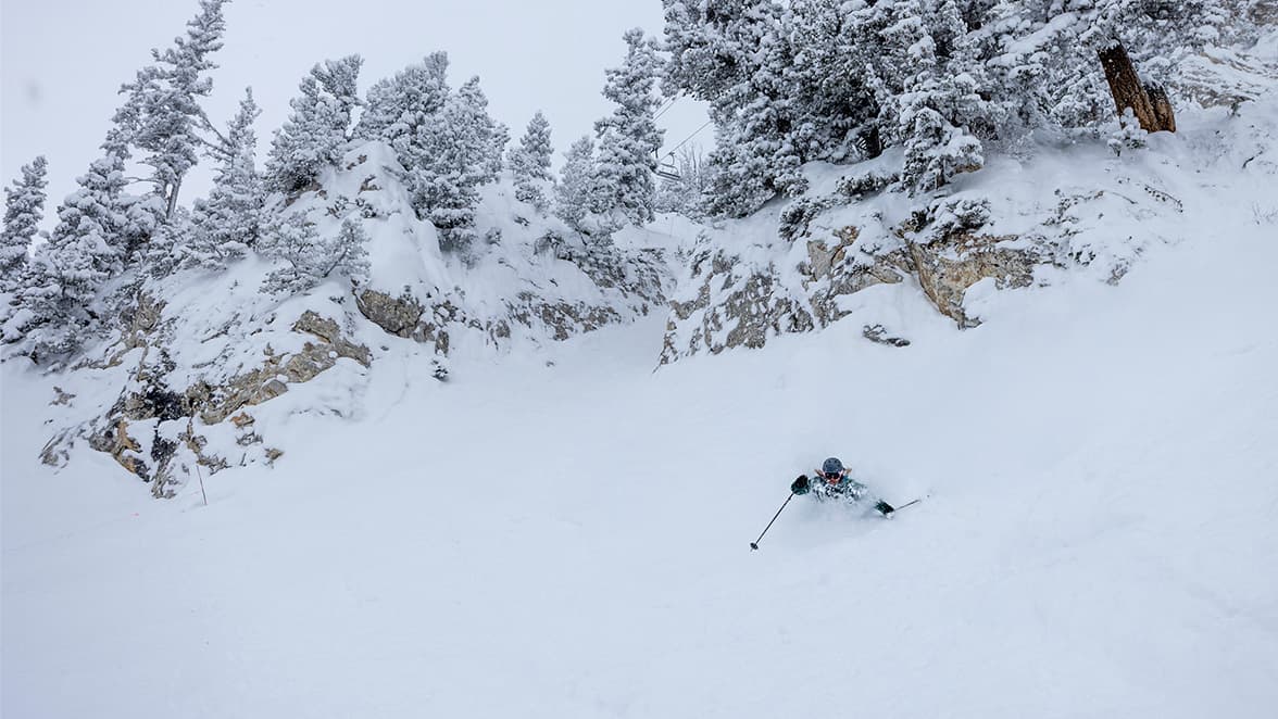 Skier in chest deep powder with a cliff and chairlift in the background
