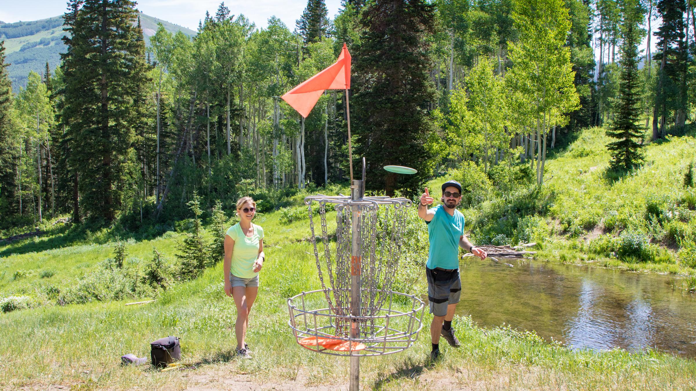 A couple playing disc golf throwing a disc at the basket