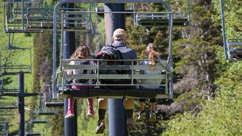 A father with two children riding up the chairlift in the summer