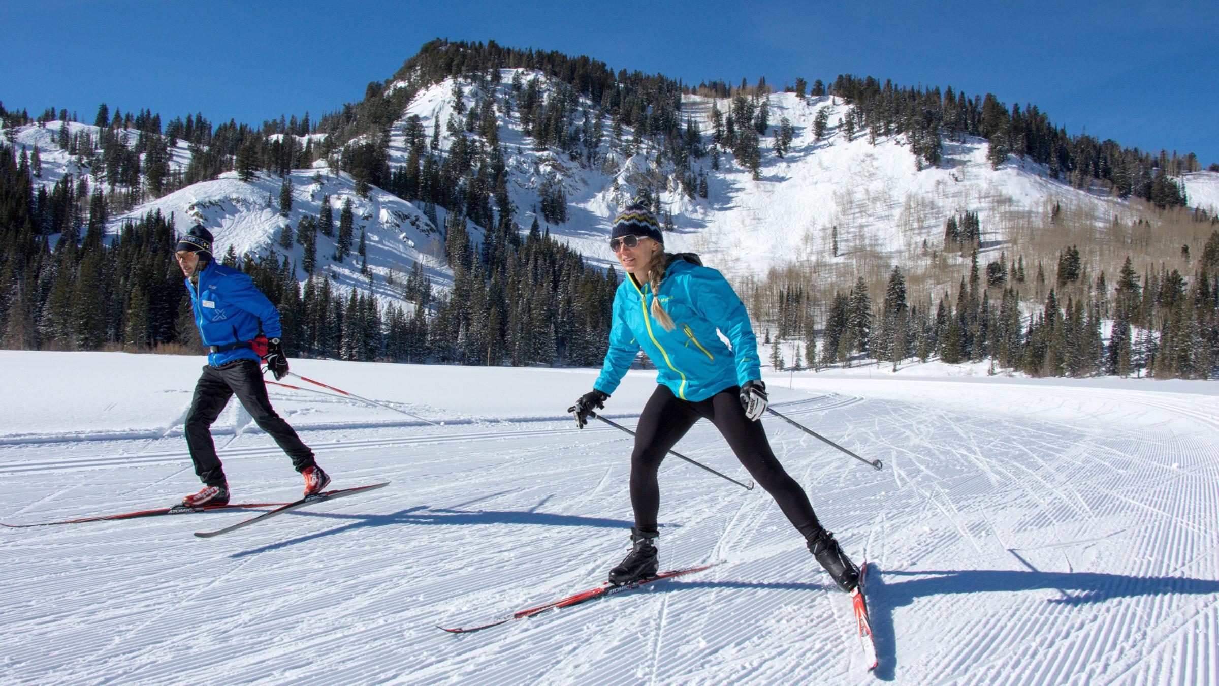 A man and women Nordic skiing on groomed trails with blue sky
